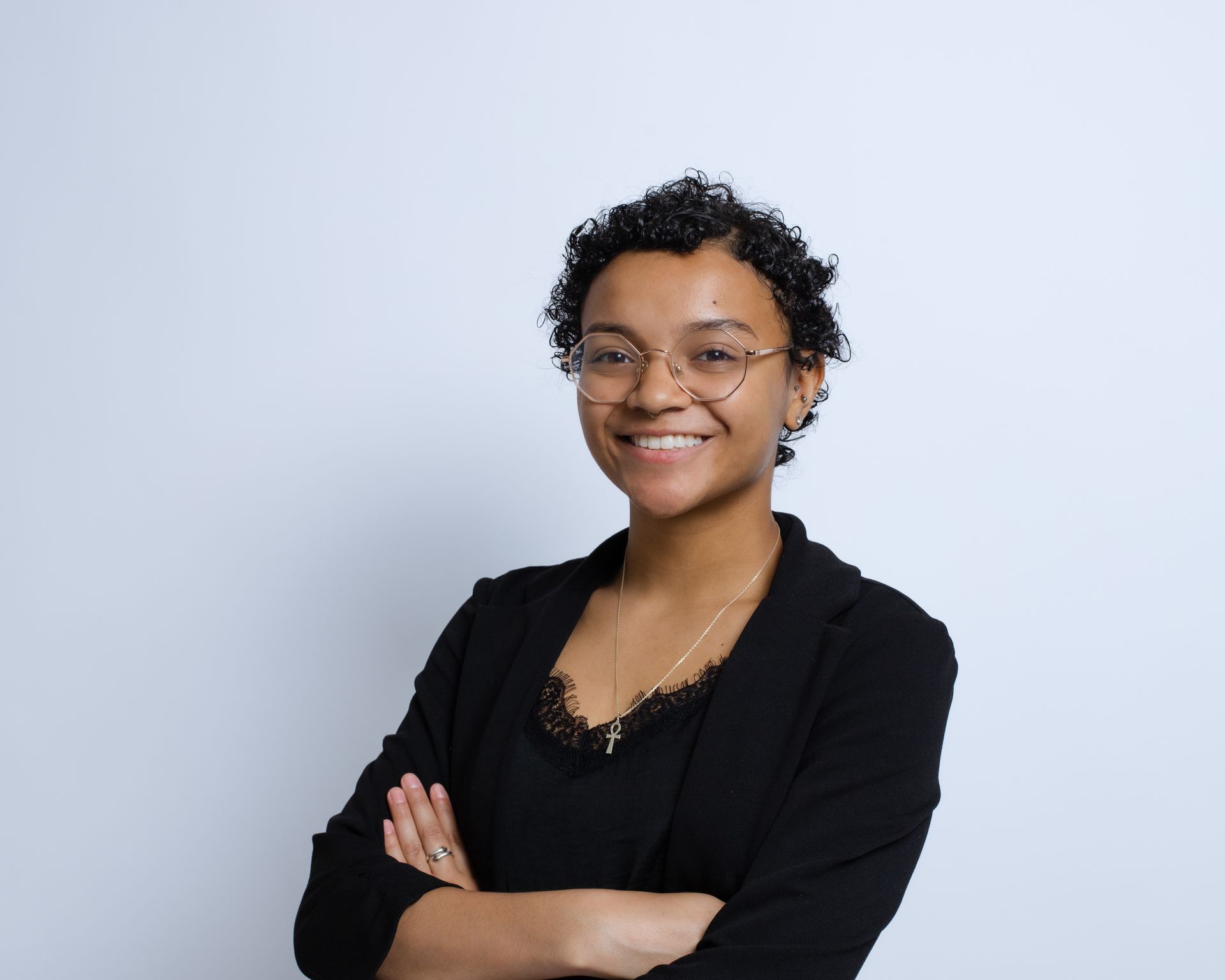 A woman wearing glasses and a black jacket is smiling with her arms crossed.