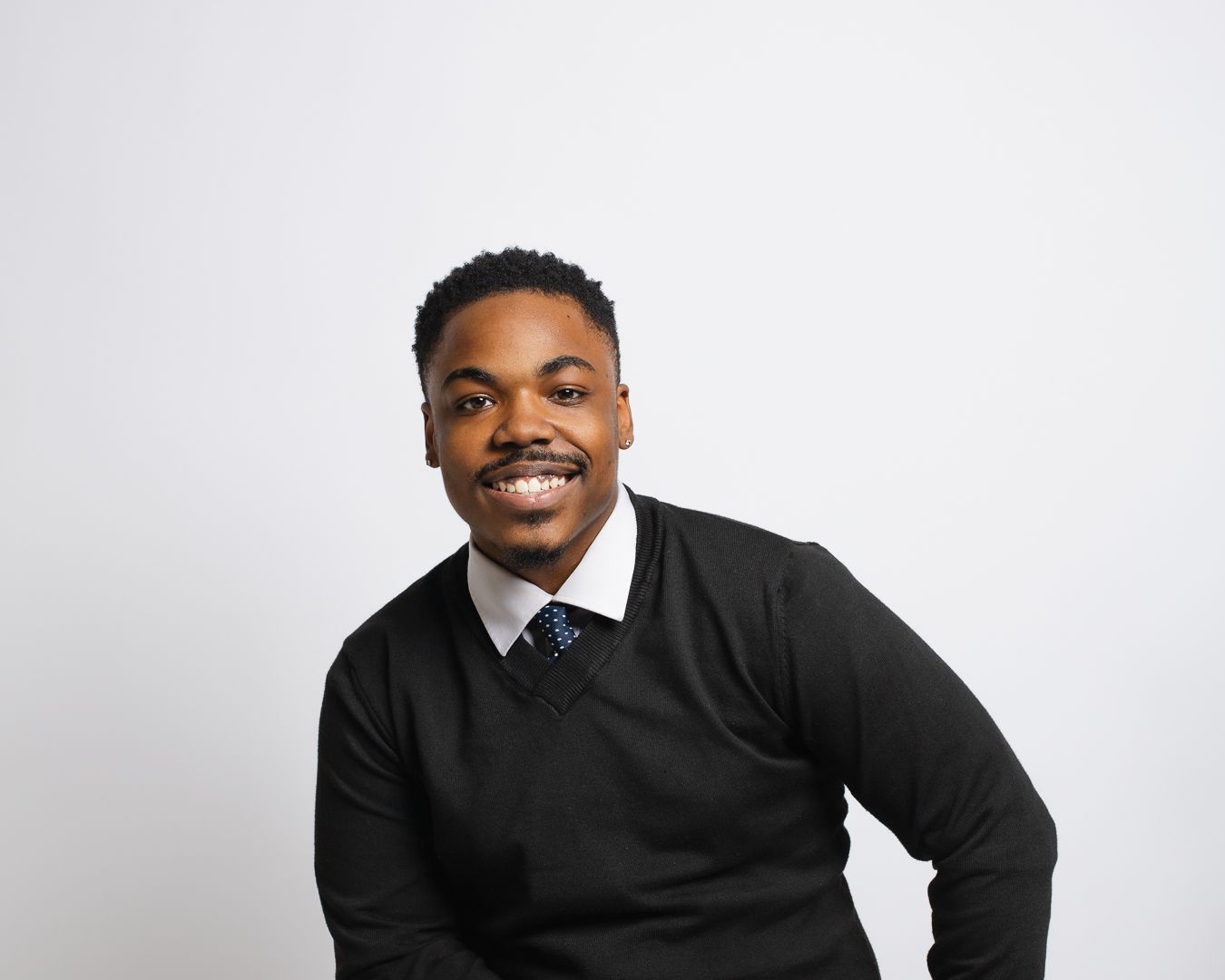 A man in a black sweater and tie is smiling for the camera.