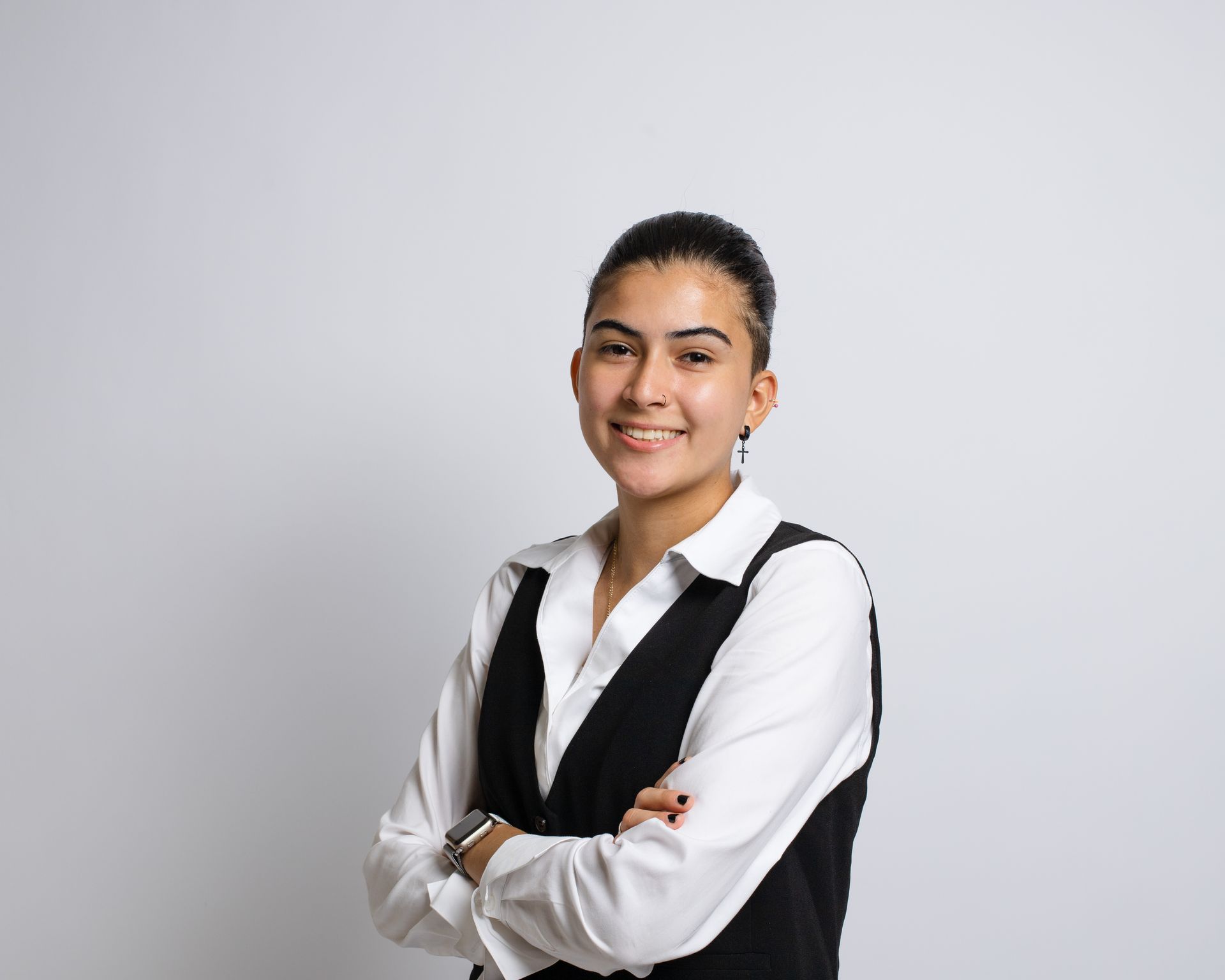 A woman in a white shirt and black vest is standing with her arms crossed.
