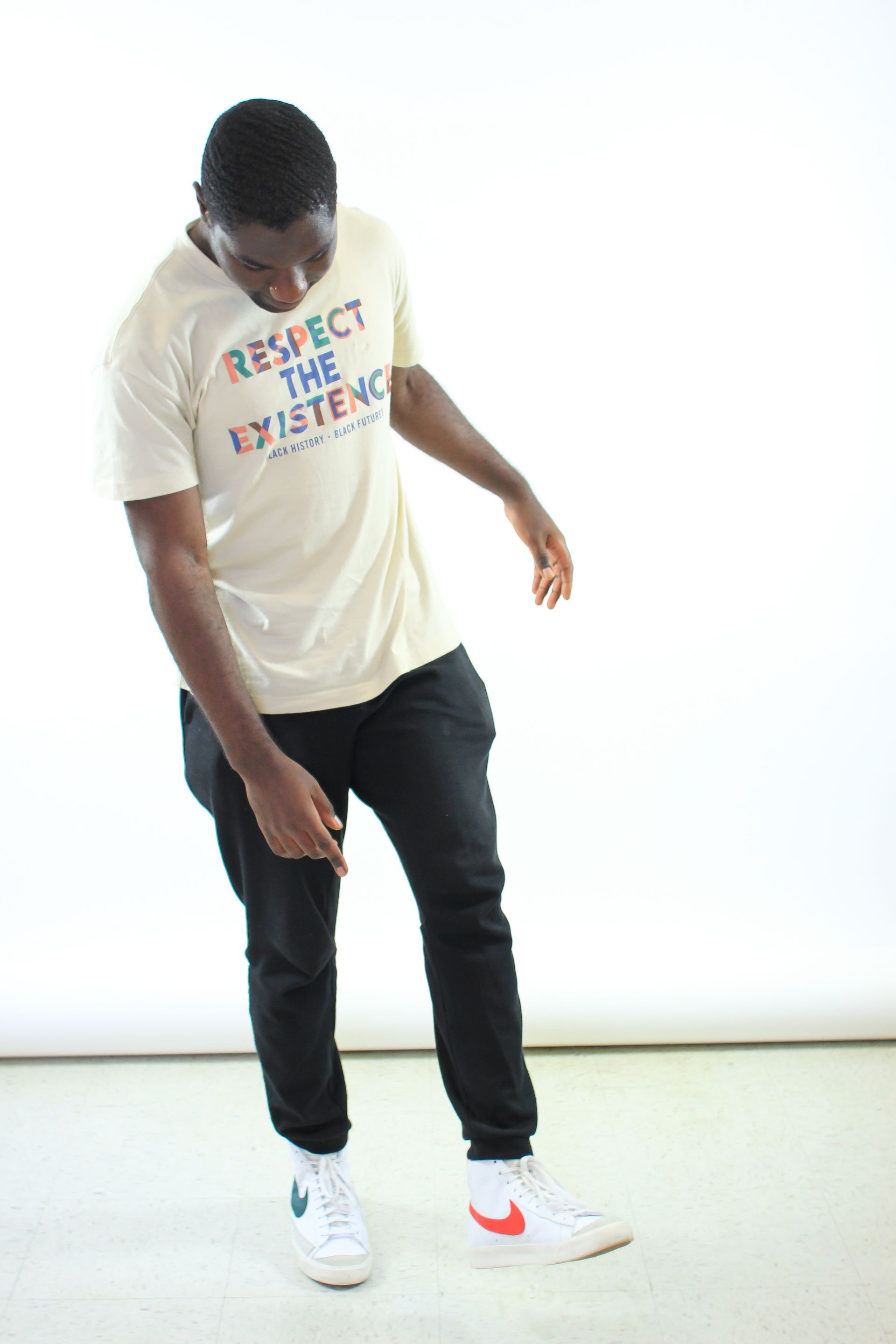 A man wearing a t-shirt that says respect the existence is standing on one leg.