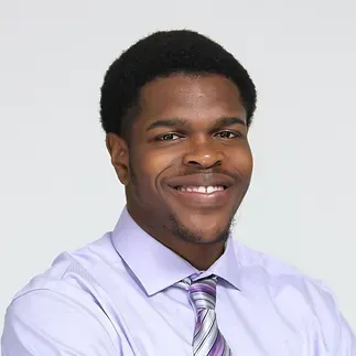 A man in a purple shirt and tie is smiling for the camera.
