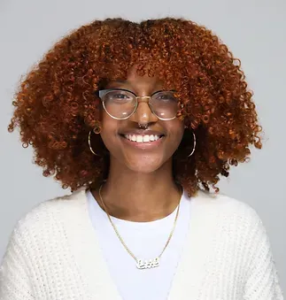 A woman with curly hair and glasses is smiling for the camera.