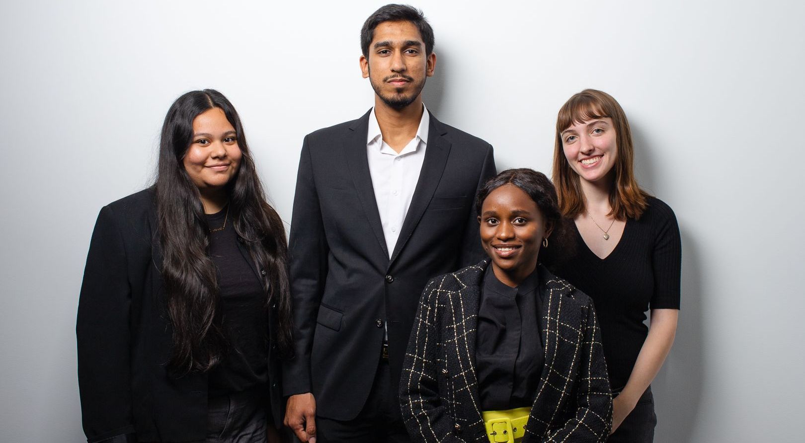 A group of people standing next to each other in front of a white wall.