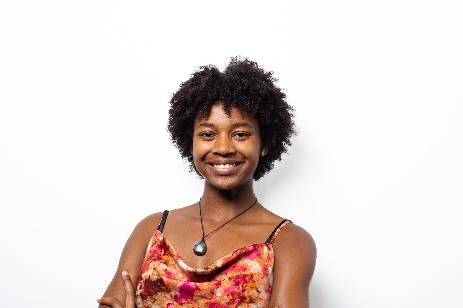 A woman with curly hair is smiling and wearing a necklace.