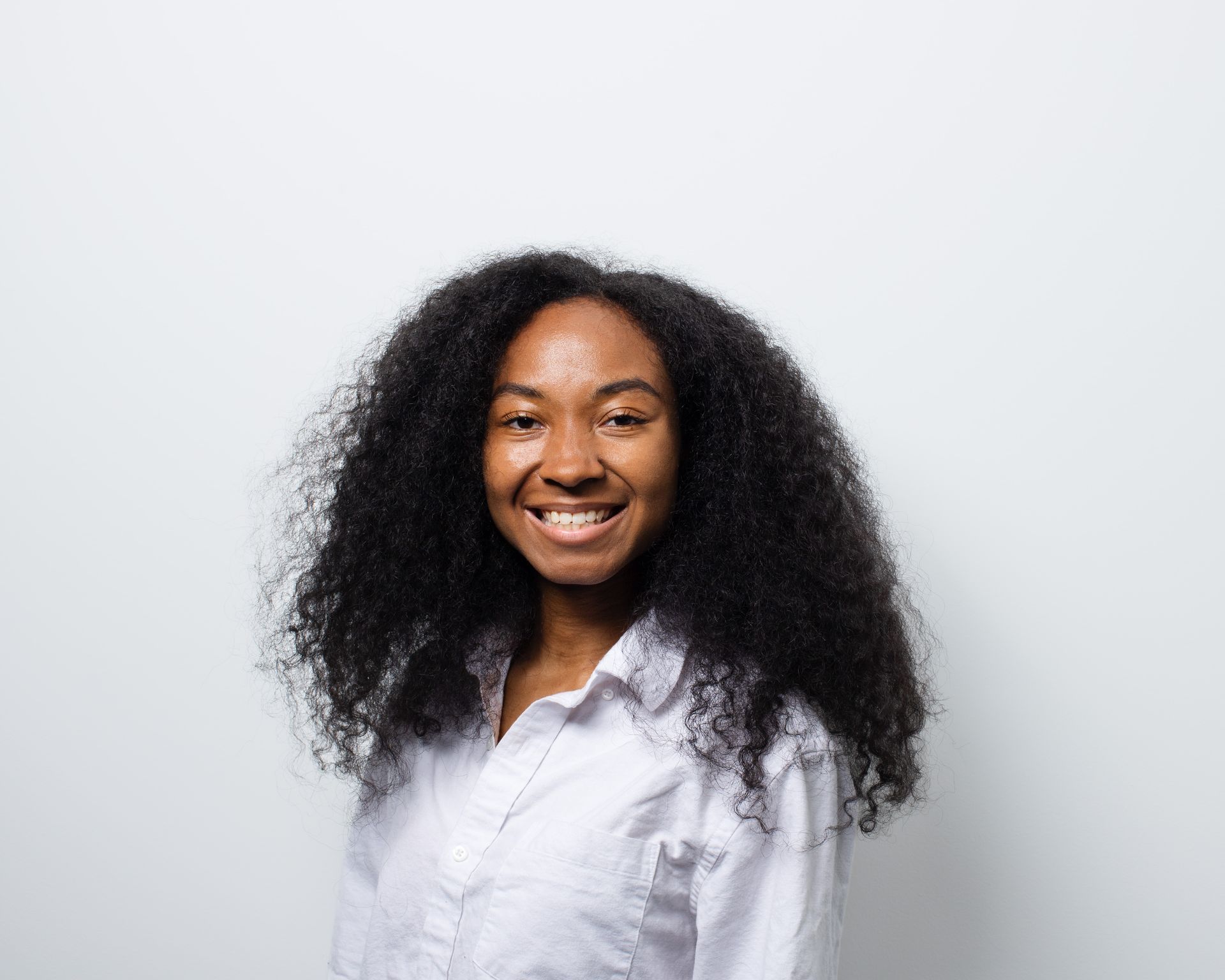 A woman with curly hair is smiling and wearing a white shirt.
