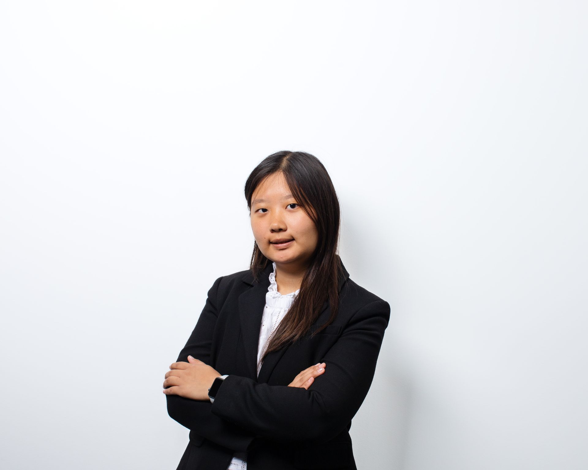 A woman in a black suit is standing with her arms crossed in front of a white wall.