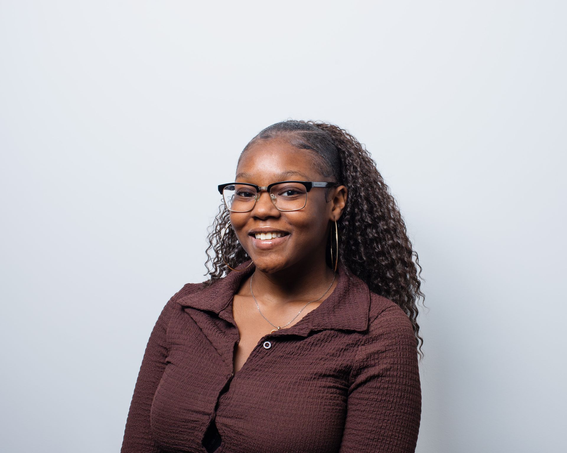 A woman wearing glasses and a brown shirt is smiling for the camera.