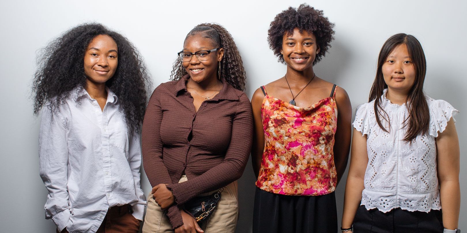 Four women are standing next to each other in front of a white wall.