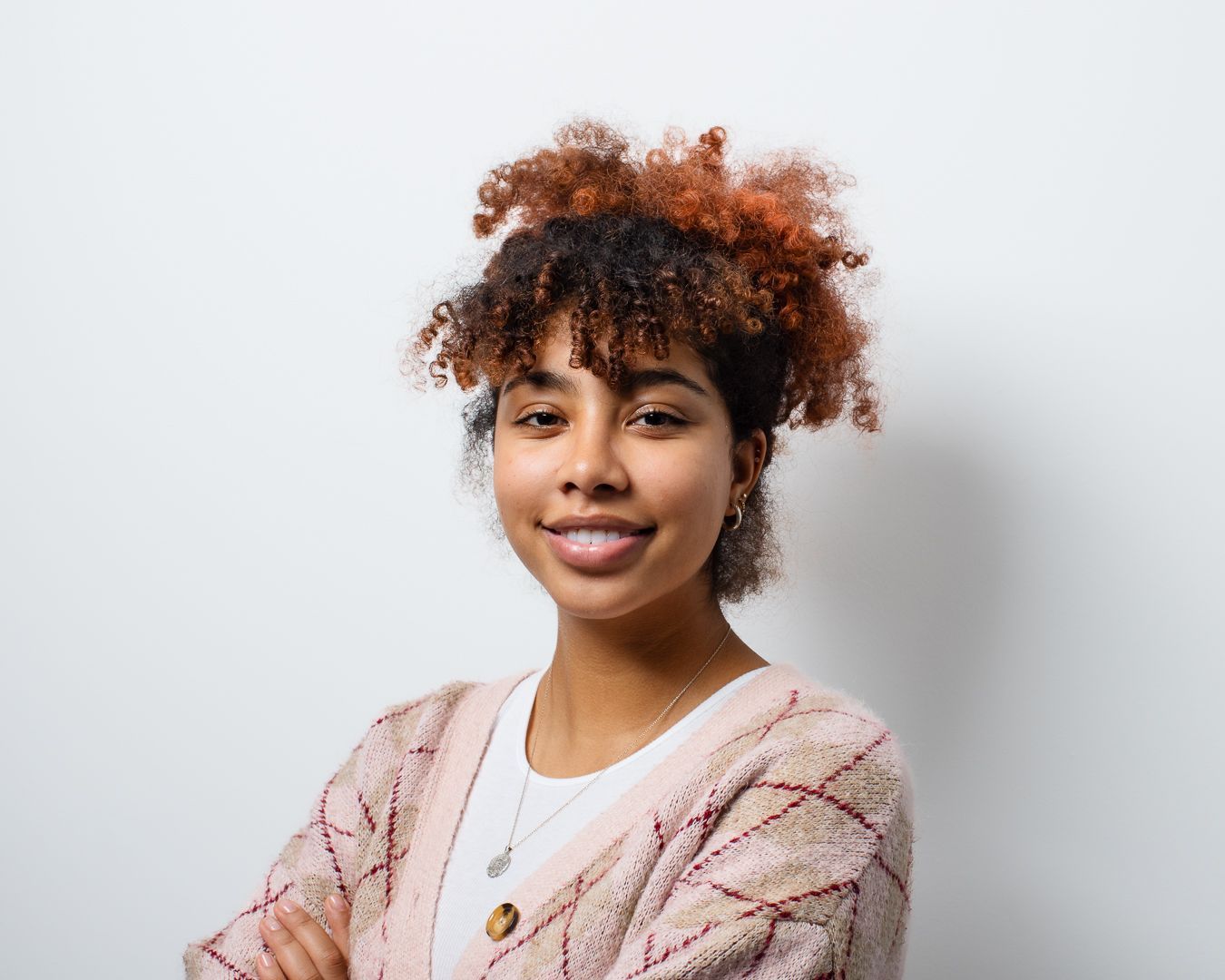 A woman with curly hair is standing with her arms crossed and smiling.