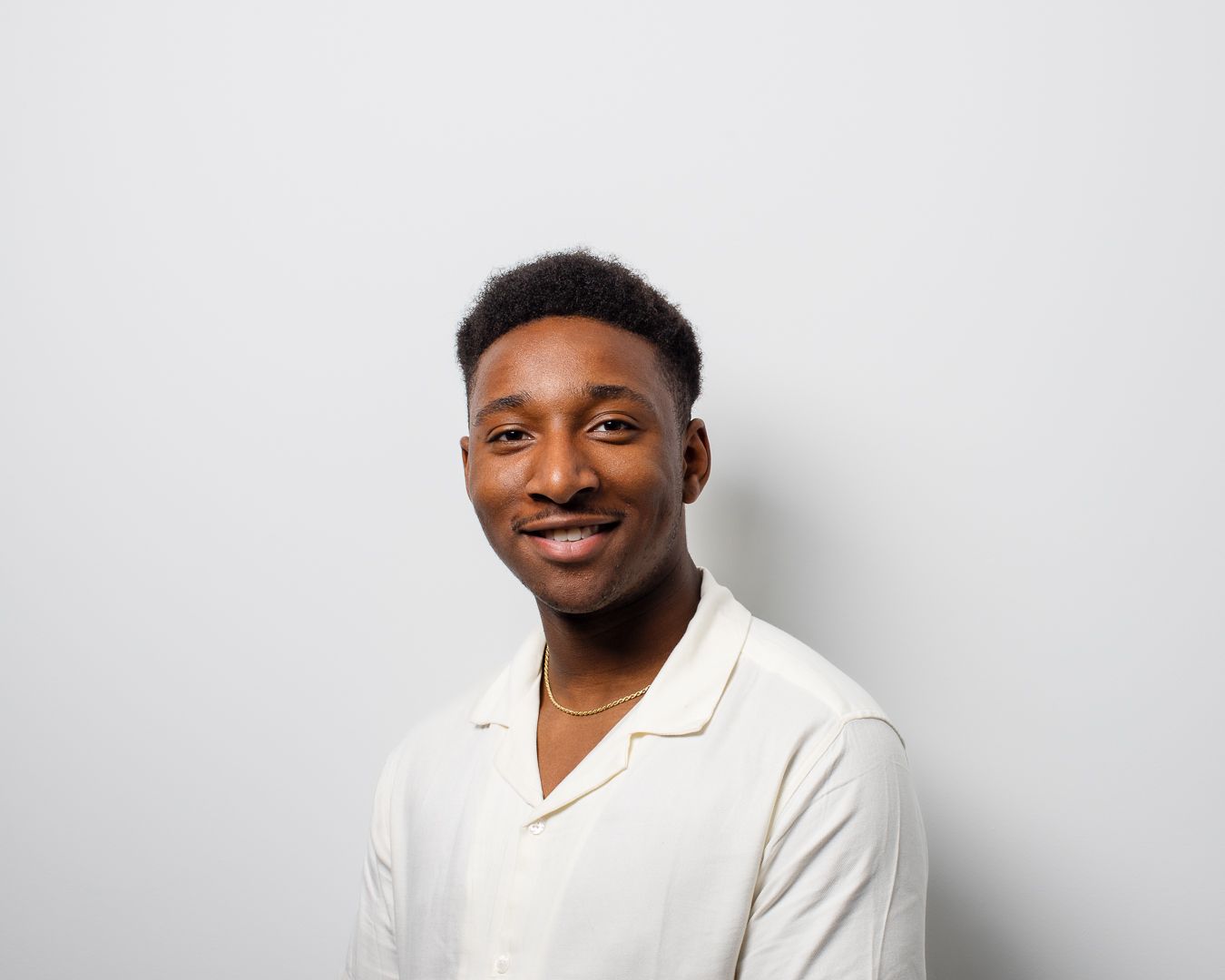 A young man in a white shirt is smiling and looking at the camera.