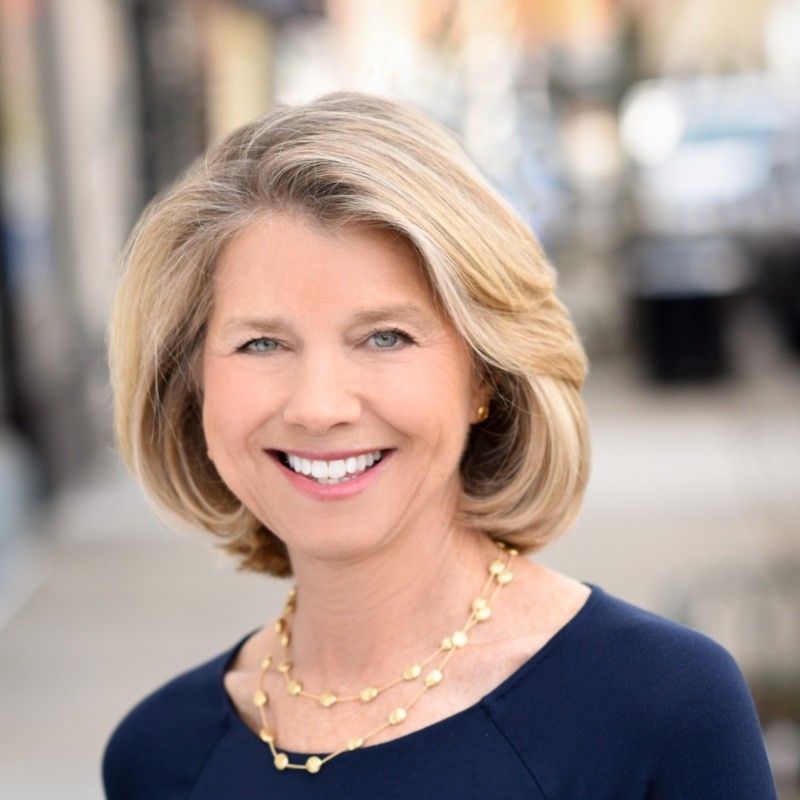 A woman wearing a blue shirt and a gold necklace smiles for the camera