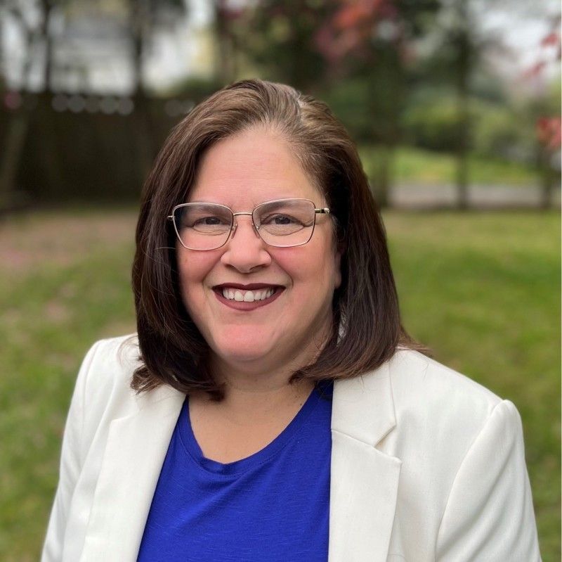 A woman wearing glasses and a blue shirt is smiling for the camera.