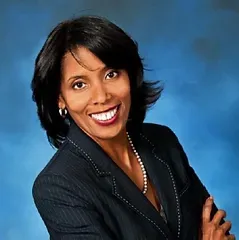A woman in a suit and pearls is smiling for the camera.