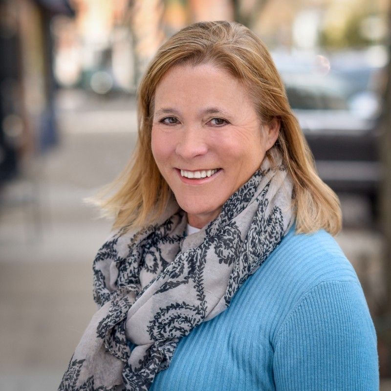 A woman wearing a blue sweater and a scarf is smiling for the camera.