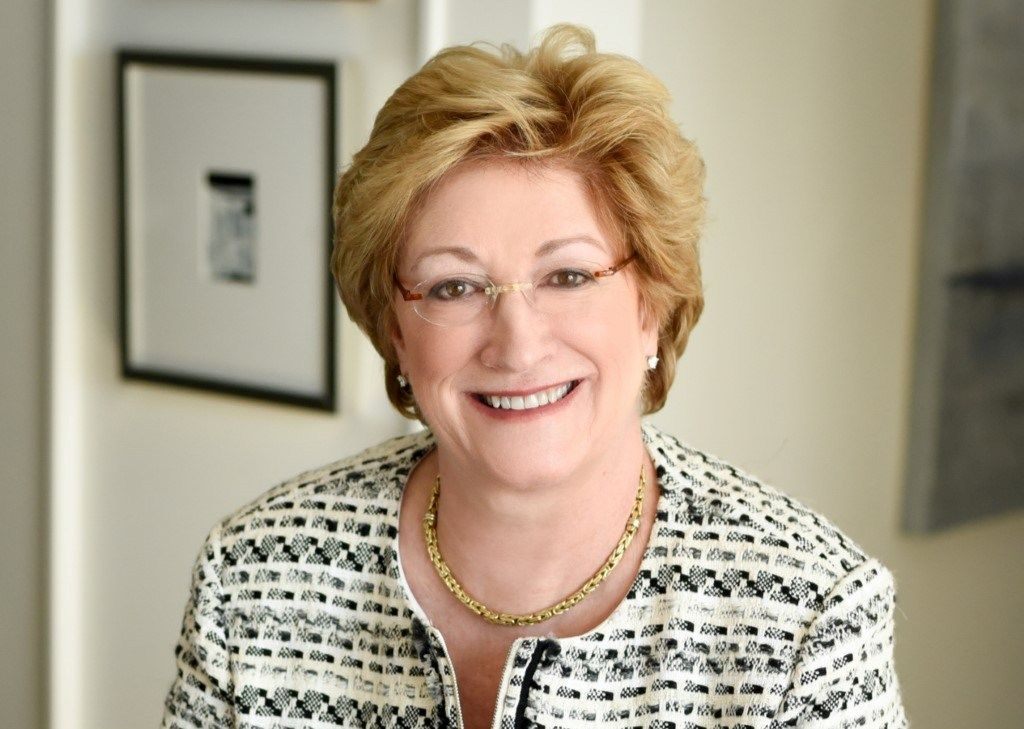 A woman wearing glasses and a necklace is smiling for the camera.