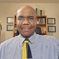 A man in a striped shirt and tie is standing in front of a bookshelf.