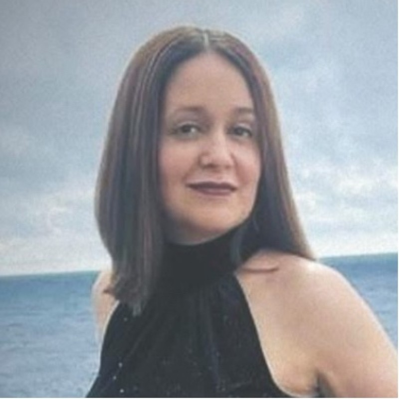 Portrait of a woman in a black halter top standing by the ocean with a cloudy sky behind her