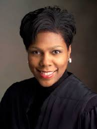 Formal studio portrait of a smiling person in a black robe against a neutral background