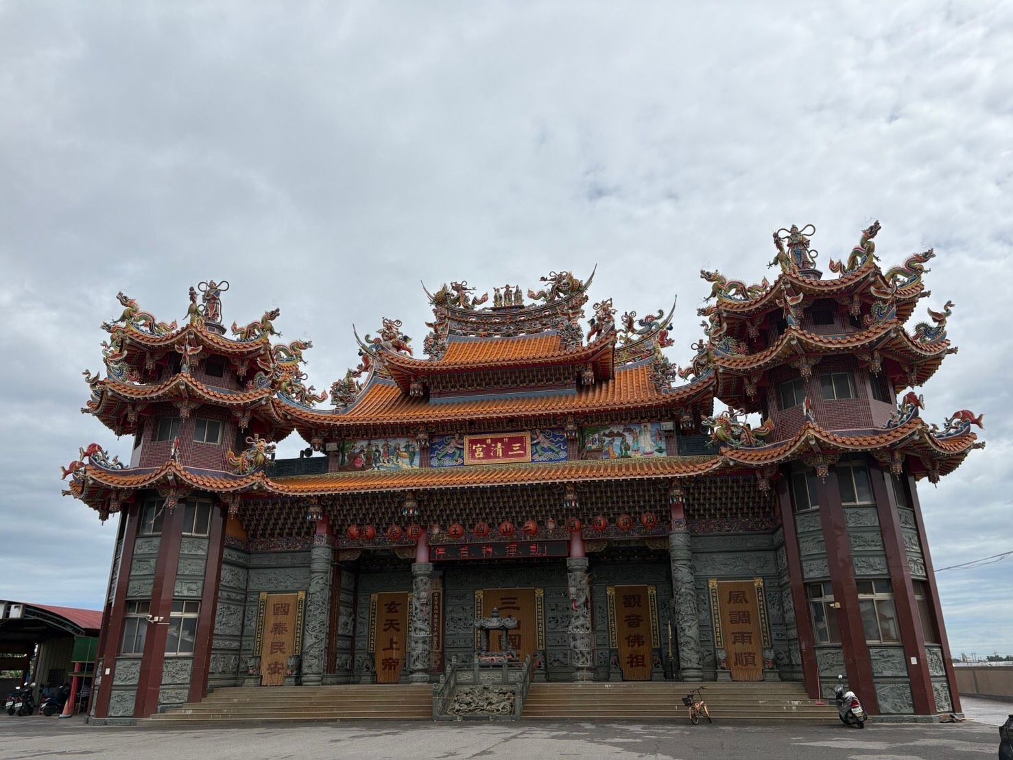 在陰雲密佈的天空下，一座裝飾華麗的中國寺廟大門矗立著，紅色的柱子上雕刻著龍的圖案。