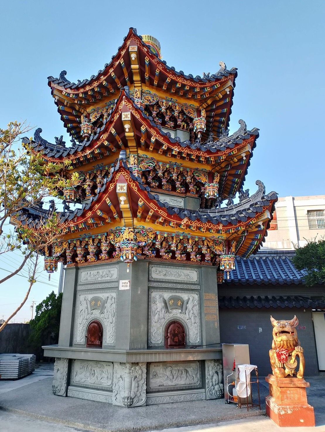 華麗的多層中式寶塔寺廟，紅金相間的屋簷，旁邊有一尊守護獅像。