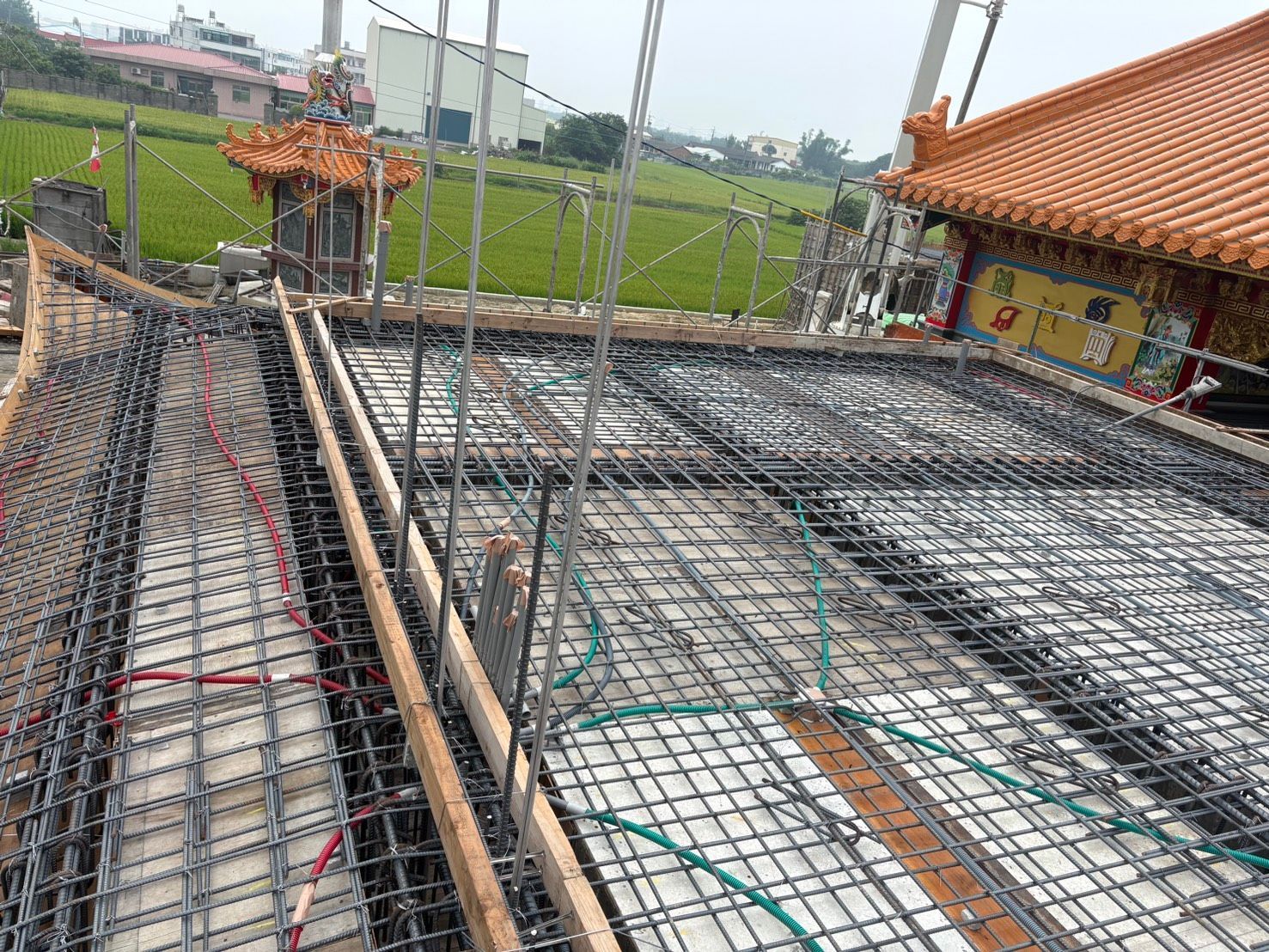 施工中建築屋頂上的鋼筋網格和模板，背景是綠色的田野。