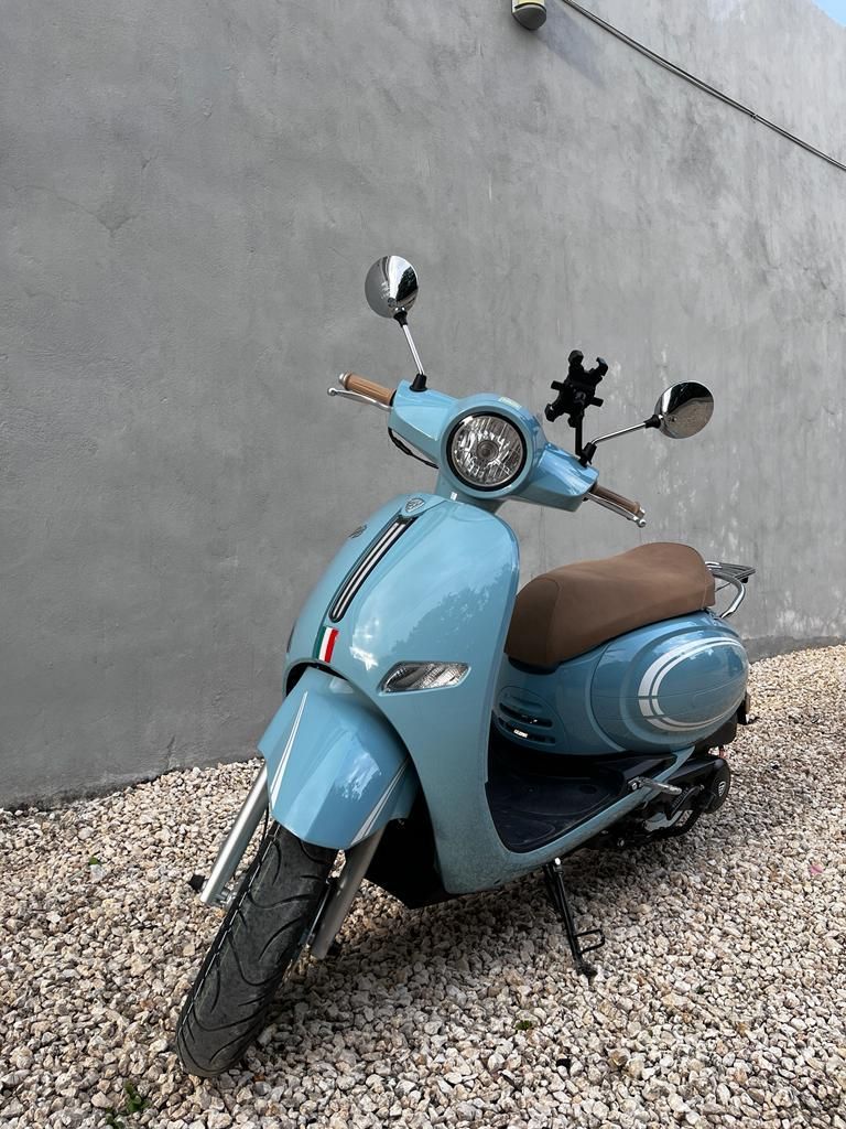 Un scooter azul está estacionado sobre grava frente a un muro.