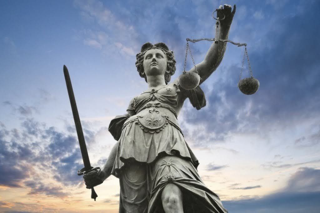 Statue of Lady Justice with scales and sword, set against a sky with clouds.
