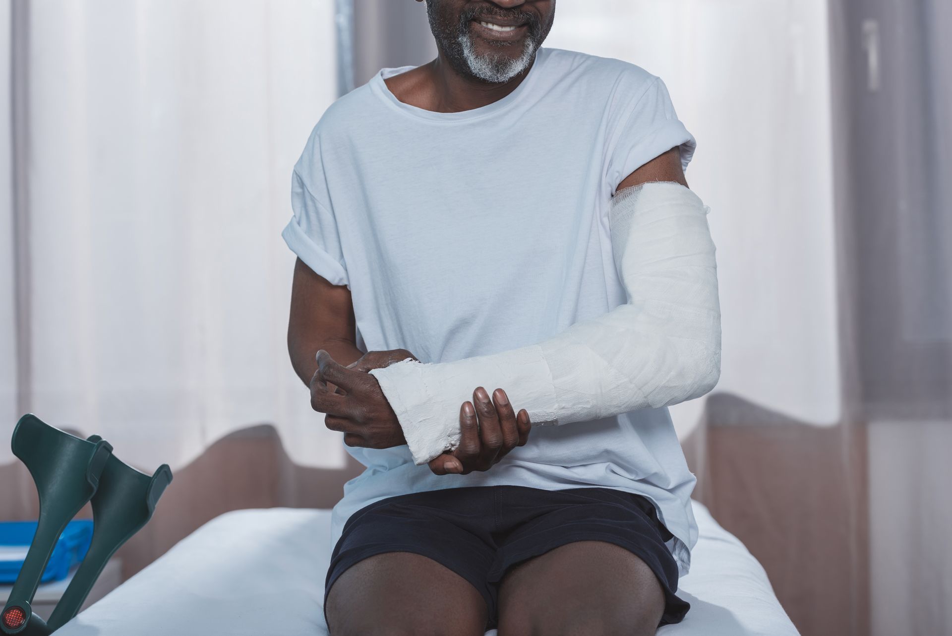 A man with a cast on his arm is sitting on a bed.