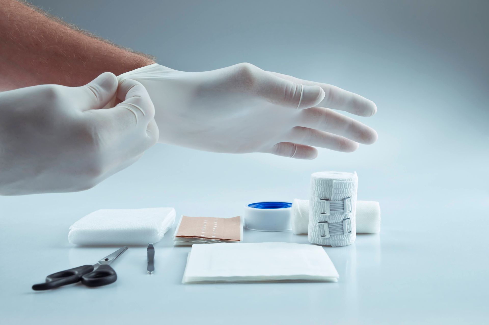 A person is putting on gloves next to a first aid kit.