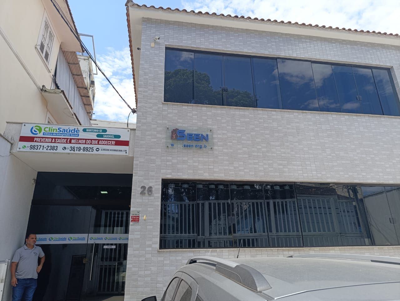 Um homem está parado em frente a um prédio com um carro estacionado na frente.