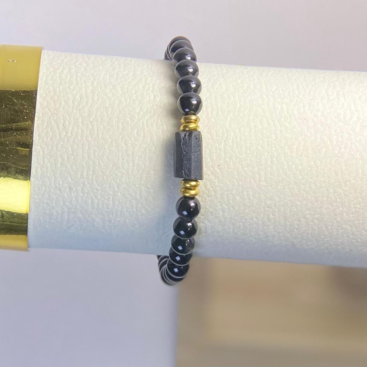 Un anillo compuesto por pequeñas cuentas oscuras y pulidas, con una cuenta cilíndrica gris