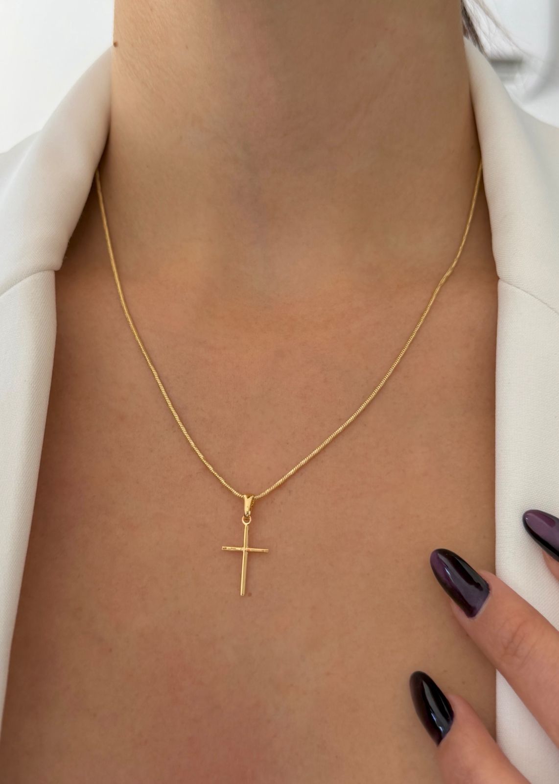 Una persona que lleva un sencillo colgante de cruz de oro en una delicada cadena de oro sobre una camisa blanca con cuello.