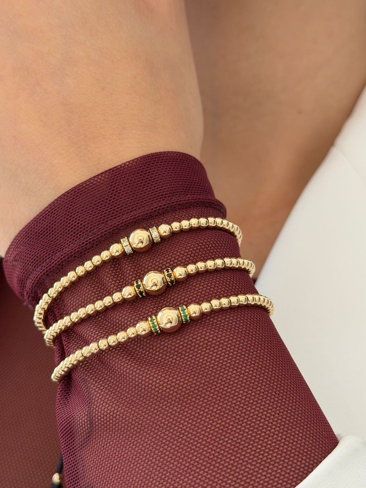 Tres pulseras ajustables con cuentas de oro, sostenidas por una mano, cada una con una cuenta central de oro