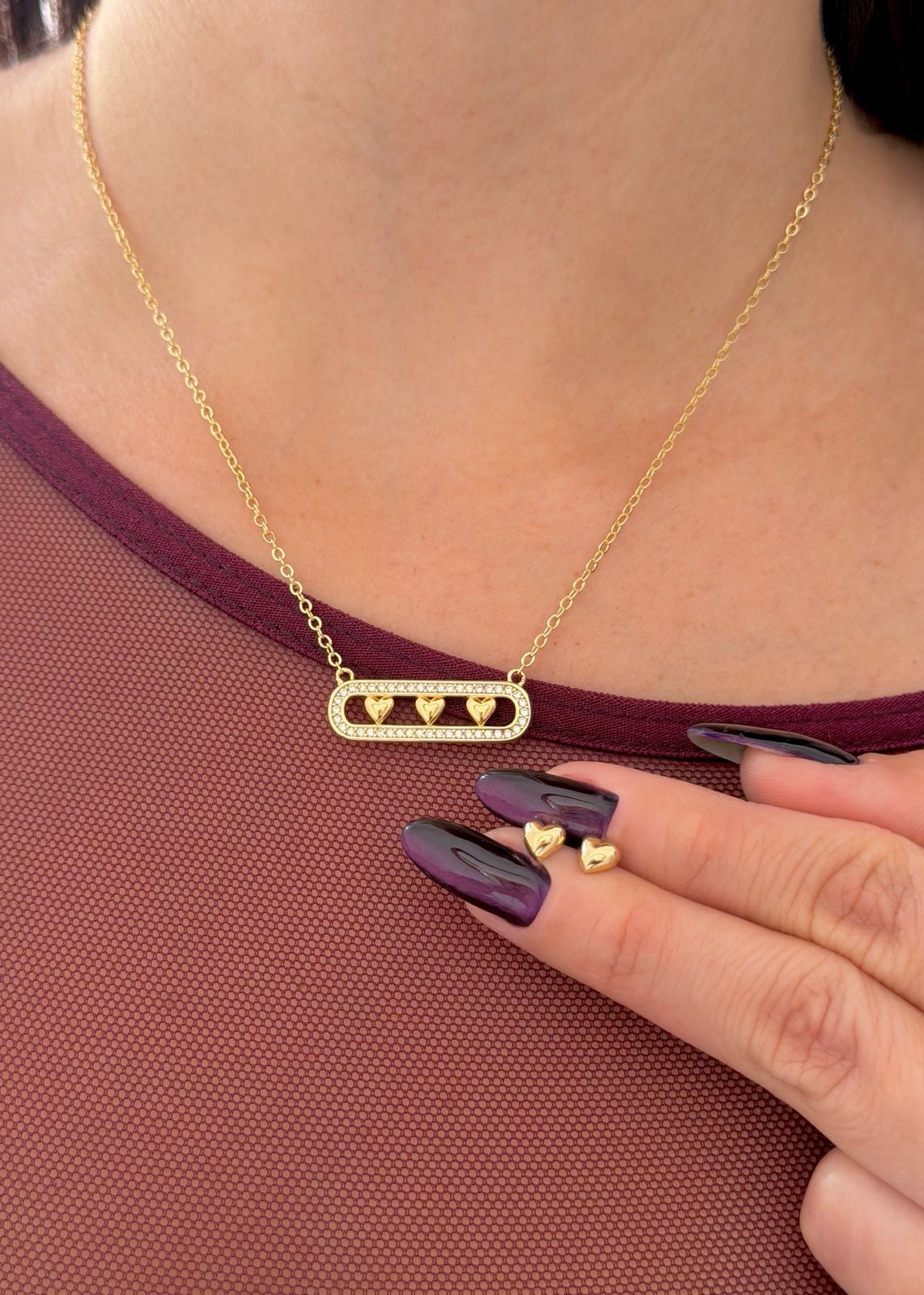 Una persona que lleva un collar con una barra de oro y tres pequeños colgantes en forma de corazón