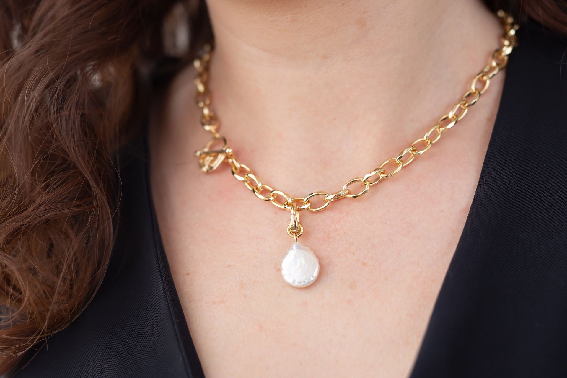 Una persona que lleva un collar de eslabones de oro con un colgante blanco en forma de lágrima.