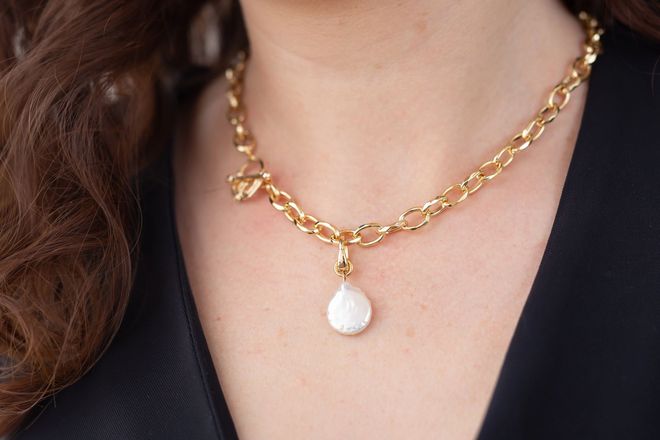 Una persona que lleva un collar de eslabones de oro con un colgante blanco en forma de lágrima.