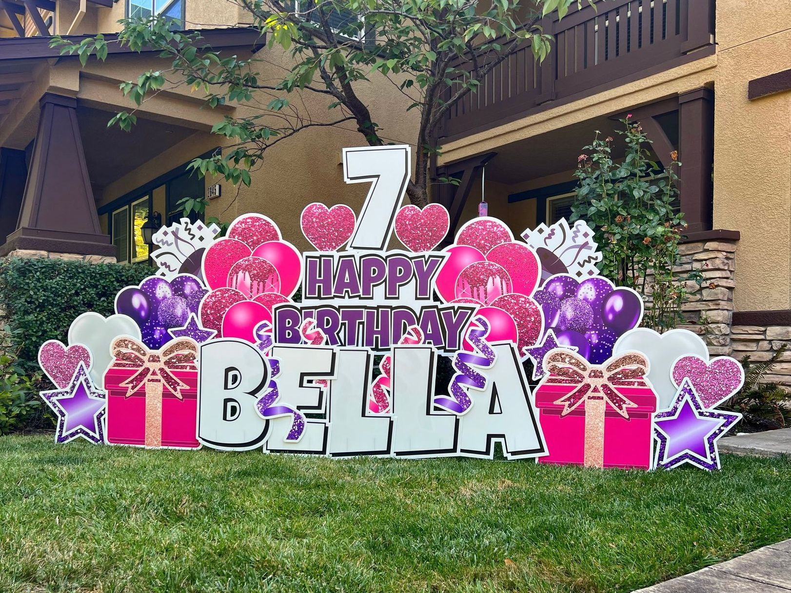 Birthday yard card display. Happy 7th birthday Bella. Pink and purple balloons, presents, stars, and hearts. 