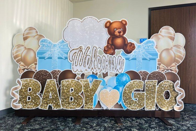 Baby yard card in brown and blue. Welcome Baby Gio with teddy bears, balloons, presents. 