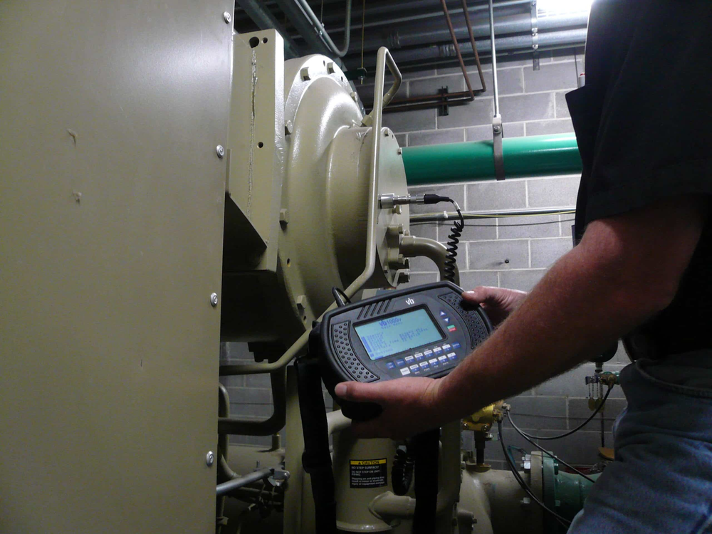 Person holding a diagnostic device, inspecting industrial machinery in a utility room.