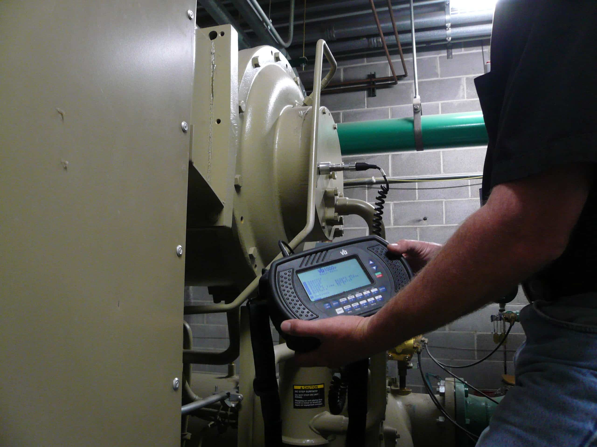 Person holding a diagnostic device, inspecting industrial machinery in a utility room.