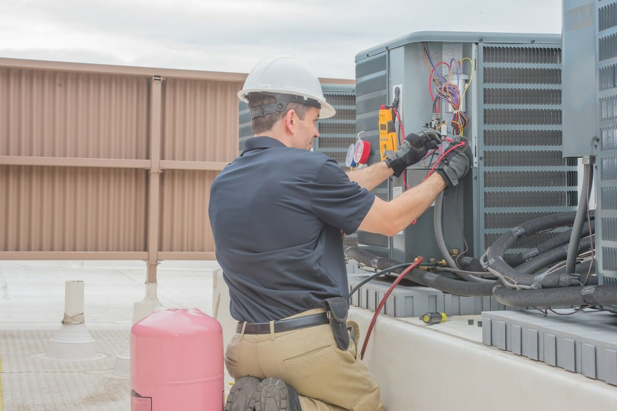 HVAC technician in hard hat working on rooftop air conditioning unit, using tools.
