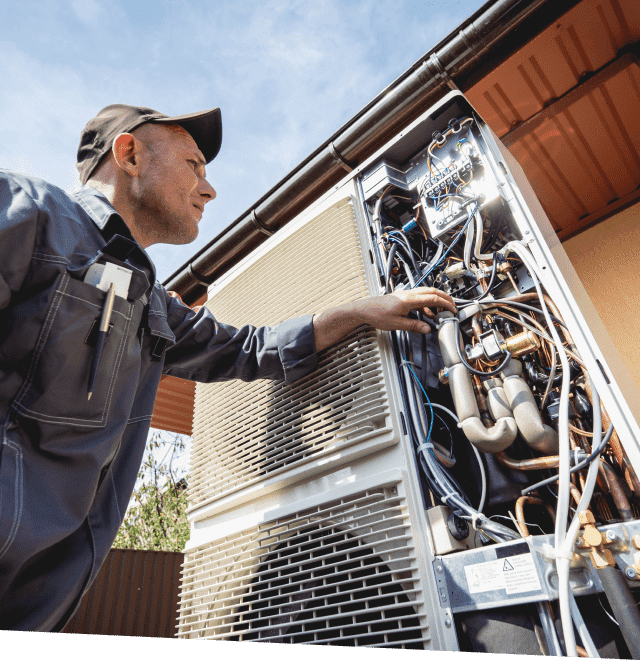 Technician in work uniform inspecting the internal components of an outdoor HVAC unit.