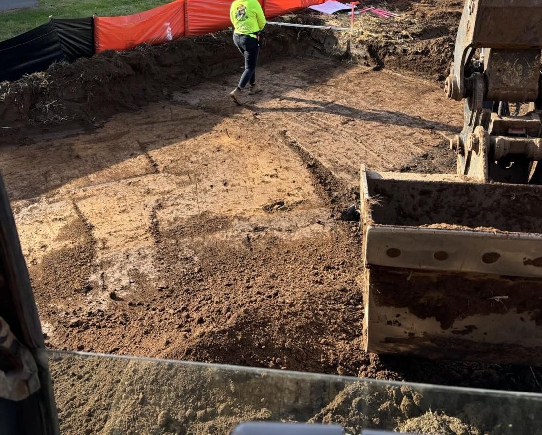 A yellow excavator is digging a hole in a dirt field.
