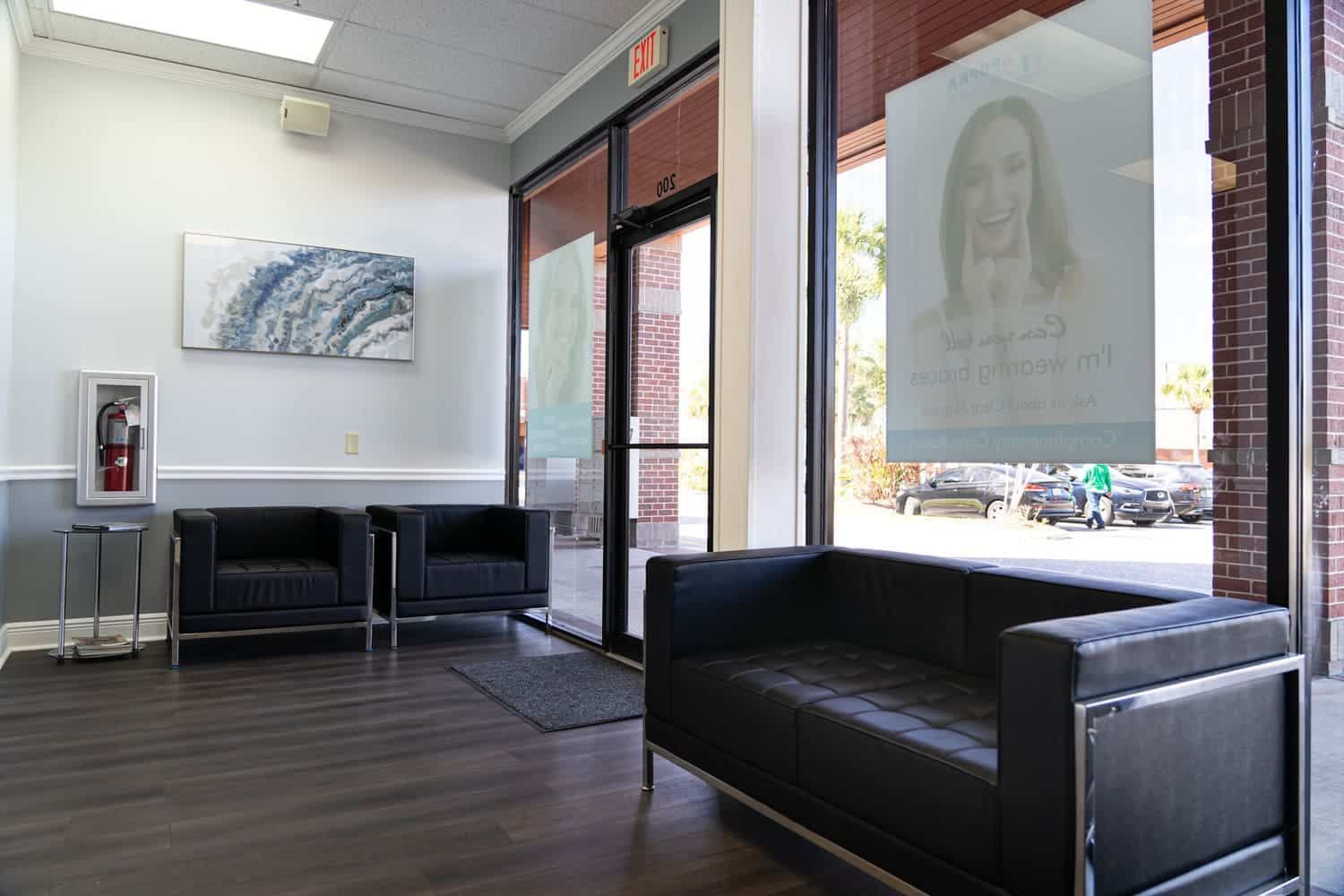 A waiting room with a couch , chairs and a painting on the wall.