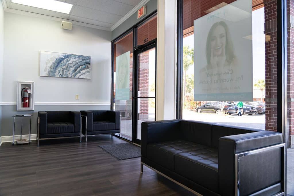A waiting room with a couch , chairs and a window.