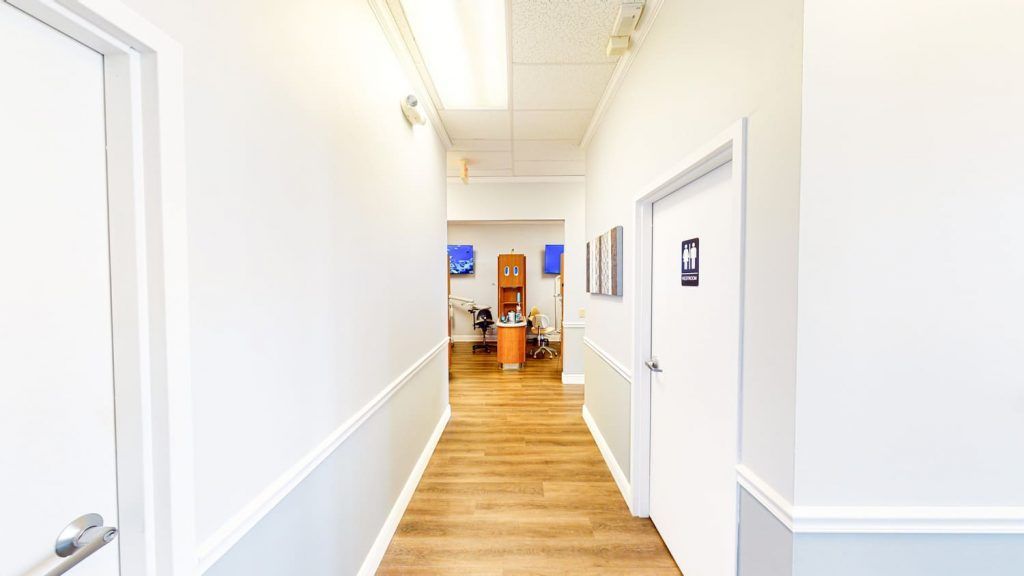 A long hallway with white walls and wooden floors leading to a room.