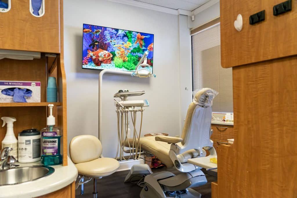 A dental office with a dental chair , sink , and television.
