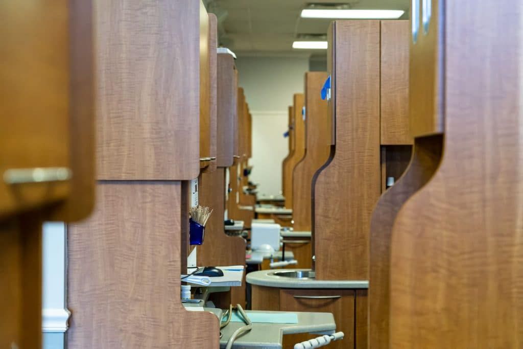 A row of dental chairs in a dental office with wooden cabinets.