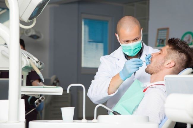 A man is sitting in a dental chair while a dentist examines his teeth.