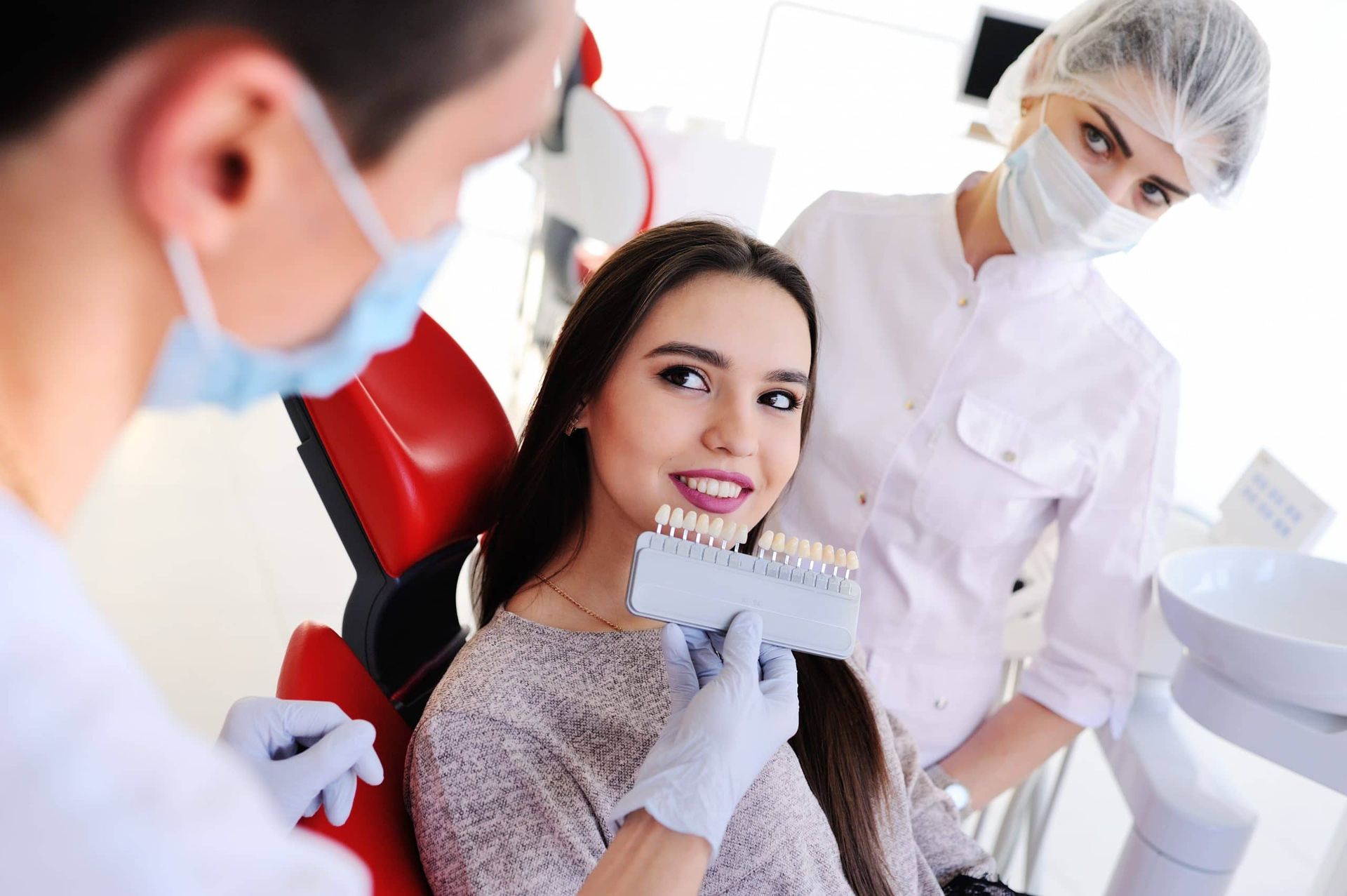 cute young girl in dentist's chair.the selection of the color of teeth A woman is sitting in a dental chair while a dentist examines her teeth.